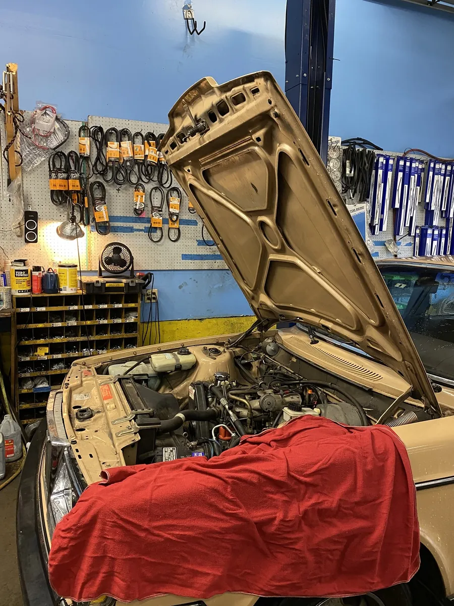 A tan Volvo 240 with its hood up in the All Vovo shop