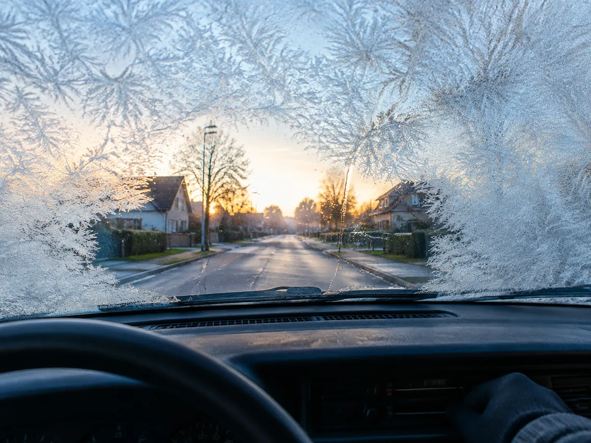 A frost-covered windshield seen from the driver's seat, clearing in the middle as the heater warms up